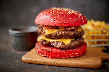 Homemade red sesame bun double bacon cheese burger. Served with french fries on wooden board.