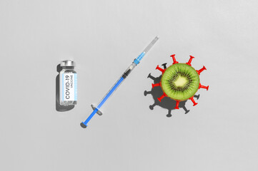 Coronavirus vaccination creative concept. Vial vaccine, medical syringe, and kiwi fruit in form virus on gray background. Top view, flat lay