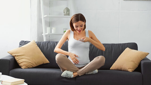 happy pregnant woman touching belly while sending voice message on cellphone