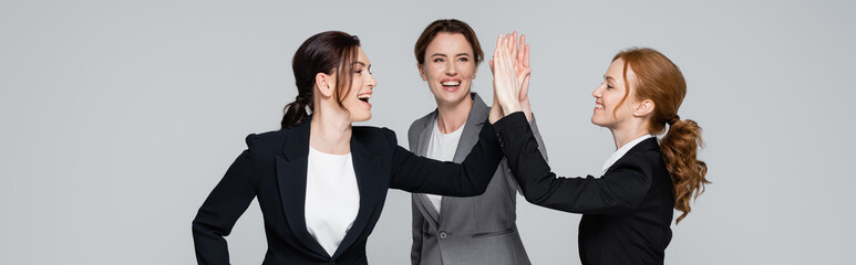 Cheerful businesswomen giving high five isolated on grey, banner