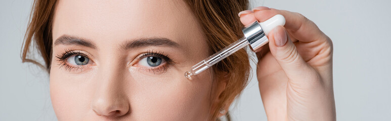 Cropped view of woman applying cosmetic serum on face isolated on grey, banner