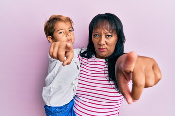 Hispanic family of mother and son hugging together with love pointing with finger to the camera and to you, confident gesture looking serious