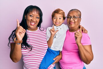 Hispanic family of grandmother, mother and son hugging together smiling with an idea or question pointing finger with happy face, number one