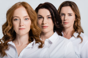 Brunette woman looking at camera near friends on blurred foreground isolated on grey