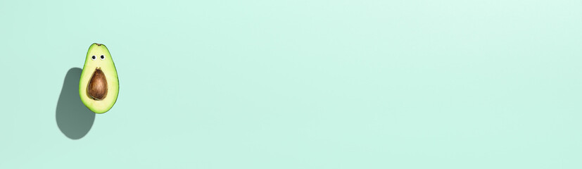 Funny half avocado with eyes, hovering over pastel turquoise color background. Minimal banner with...