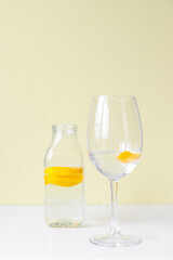 glass bottle and glass goblet with water and lemon on a light background. Lemonade, lemon juice, citrus, orange, vitamins, diet, detox, cleansing, smoothie, fresh morning, water