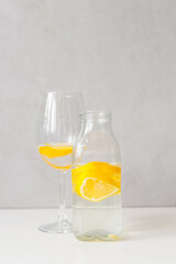 glass bottle and glass goblet with water and lemon on a light background. Lemonade, lemon juice, citrus, orange, vitamins, diet, detox, cleansing, smoothie, fresh morning, water