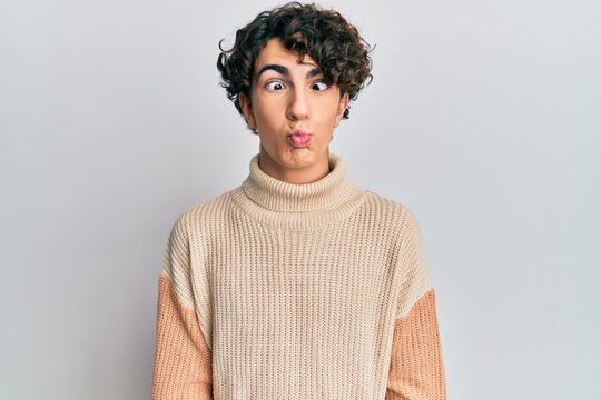 Hispanic young man wearing casual winter sweater making fish face with lips, crazy and comical gesture. funny expression.