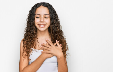 Teenager hispanic girl wearing casual clothes smiling with hands on chest with closed eyes and grateful gesture on face. health concept.