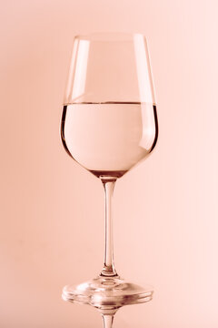 Wine glass with transparent liquid on rose background