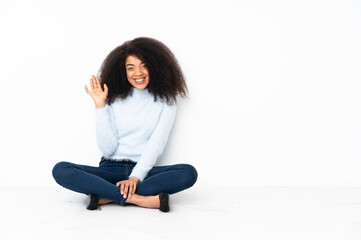 Young african american woman sitting on the floor saluting with hand with happy expression