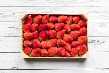 delicious red strawberries tightly arranged in a wooden box on a white wooden background - 423295482