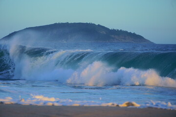 Ondas quebrando no mar na Praia de Piratininga, Niterói no Rio de Janeiro. Morro ao fundo. Fim de tarde de verão.