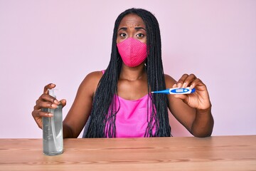 African american woman with braids wearing medical mask, hand sanitizer gel and thermometer...
