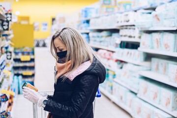 Woman in a protectivel mask and rubber gloves viewing a products label at the supermarket.