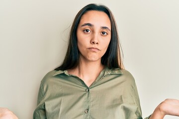 Young hispanic woman wearing casual clothes clueless and confused expression with arms and hands...