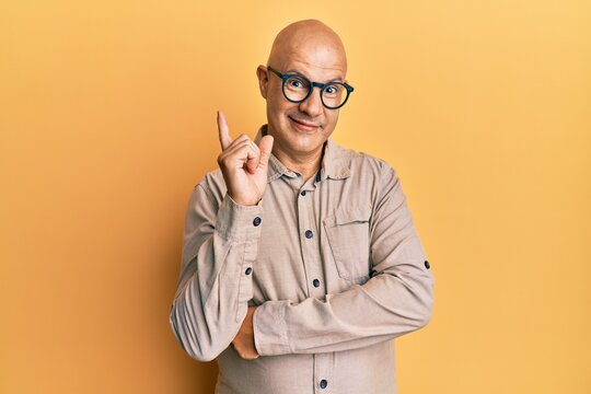 Middle age bald man wearing casual clothes and glasses with a big smile on face, pointing with hand and finger to the side looking at the camera.