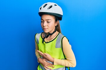 Beautiful brunette little girl wearing bike helmet and reflective vest with hand on stomach because nausea, painful disease feeling unwell. ache concept.