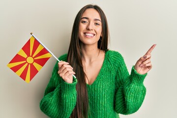 Young hispanic girl holding macedonian flag smiling happy pointing with hand and finger to the side