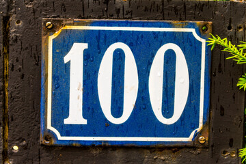 The number 100 street address sign with white characters and a blue background.