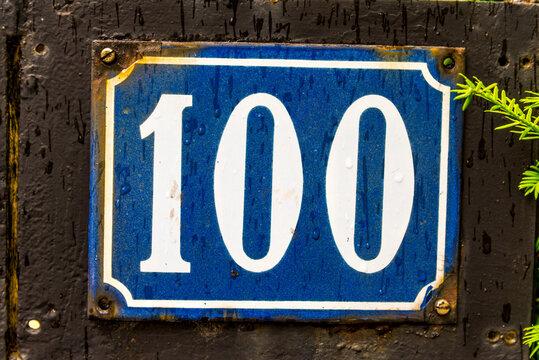 The Number 100 Street Address Sign With White Characters And A Blue Background.