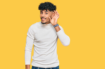 Young arab man wearing casual winter sweater smiling with hand over ear listening an hearing to...