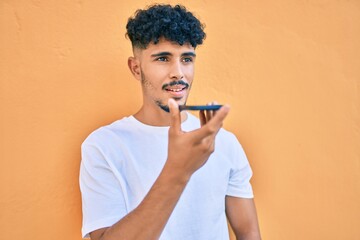 Young arab man sending audio message using smartphone at city