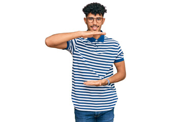 Young arab man wearing casual clothes and glasses gesturing with hands showing big and large size sign, measure symbol. smiling looking at the camera. measuring concept.