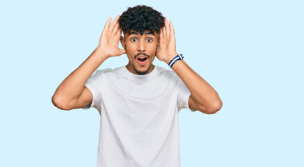 Young arab man wearing casual white t shirt smiling cheerful playing peek a boo with hands showing face. surprised and exited