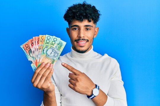 Young arab handsome man holding australian dollars smiling happy pointing with hand and finger