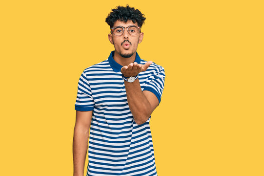 Young arab man wearing casual clothes and glasses looking at the camera blowing a kiss with hand on air being lovely and sexy. love expression.
