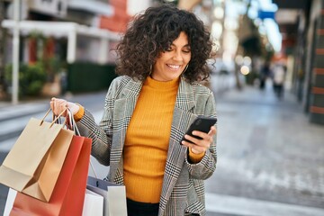 Young hispanic woman going shopping and using smatphone at the city.