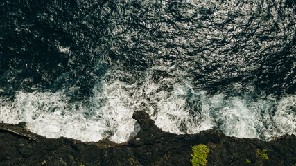 Aerial shot of waves crashing into a Hawaiian lava rock coast. drone