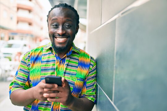 Young african american man using smartphone leaning on the wall at street of city.