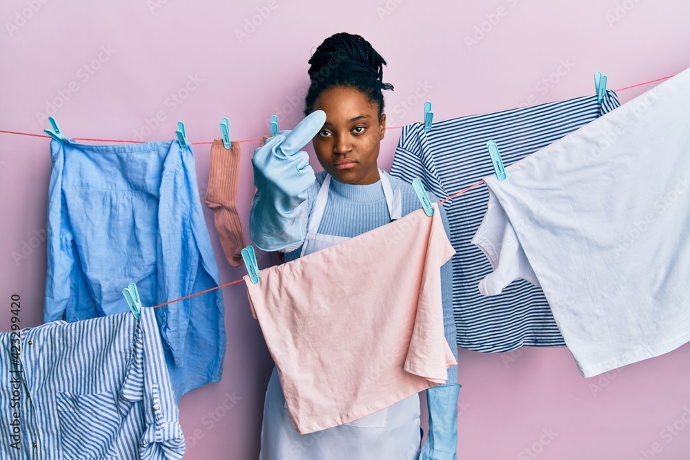 Poster african american woman with braided hair washing clothes at clothesline showing middle finger, impol