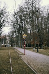 tram stop sign of public transport next to the railway in the centre of a city park forest with an empty path leading next to it