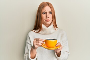 Young irish woman drinking a cup of coffee relaxed with serious expression on face. simple and natural looking at the camera.