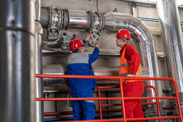 Two Power Plant Workers in Personal Protective Equipment Turning the Valve on Industrial Piping