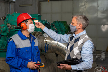 Manager Wearing Protective Face Mask and Measuring Body Temperature of Worker with Infrared Thermometer at the Factory