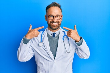 Handsome middle age man wearing doctor uniform and stethoscope smiling cheerful showing and pointing with fingers teeth and mouth. dental health concept.