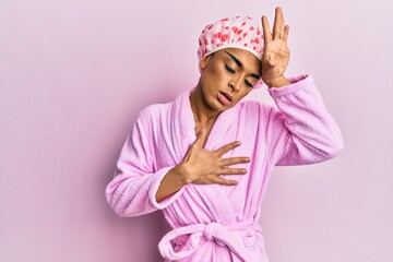 Hispanic man wearing make up wearing shower towel cap and bathrobe touching forehead for illness and fever, flu and cold, virus sick