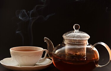 glass transparent teapot with tea leaves and a mug with tea on a saucer 