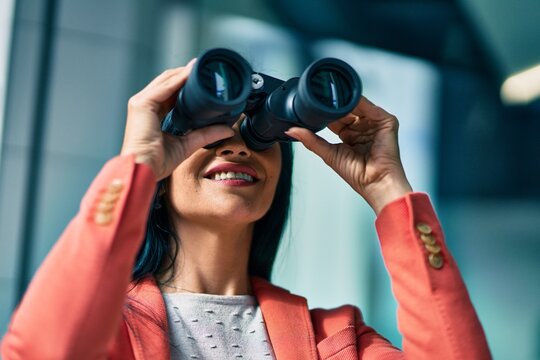 Young beautiful businesswoman smiling happy looking for new opportunities using binoculars at the city.
