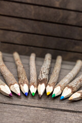 bound crayons made of real, untreated wood, unique and with real tree bark arranged in semicircle on wooden board with different colors