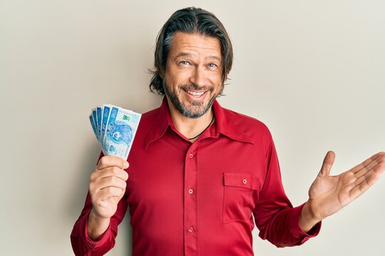 Middle age handsome man holding 50 polish zloty banknotes celebrating achievement with happy smile and winner expression with raised hand