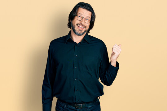 Middle age caucasian man wearing casual clothes and glasses smiling with happy face looking and pointing to the side with thumb up.
