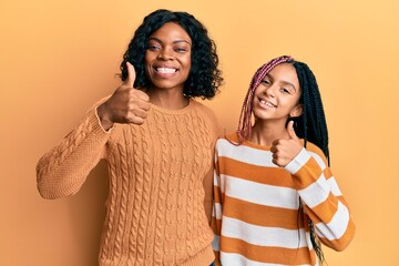 Beautiful african american mother and daughter wearing wool winter sweater doing happy thumbs up...