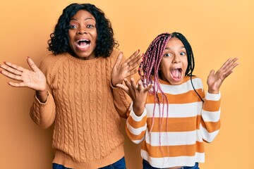 Beautiful african american mother and daughter wearing wool winter sweater celebrating crazy and...