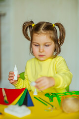 a little beautiful girl makes an application of colored paper