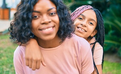 Beautiful african american mother and daughter smiling happy and hugging. Standing with smile on face standing at the park.